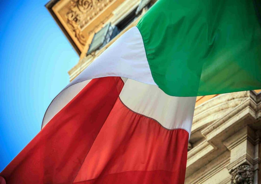 Bandeira italiana hasteada em meio a monumentos históricos com zoom na bandeira